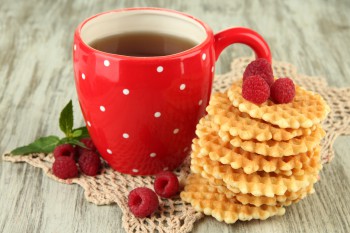 Вафли с малиной на вязаной салфетке, чай в красной чашке - фото