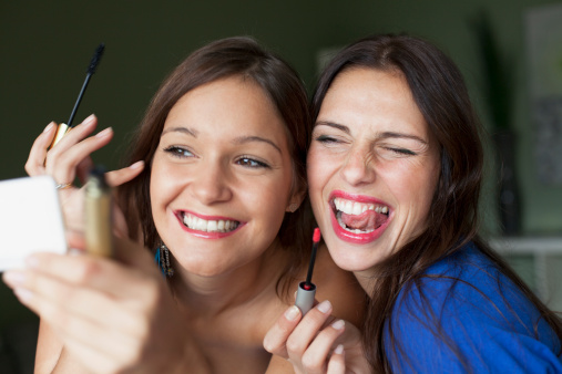 Smiling women applying makeup in mirror - фото