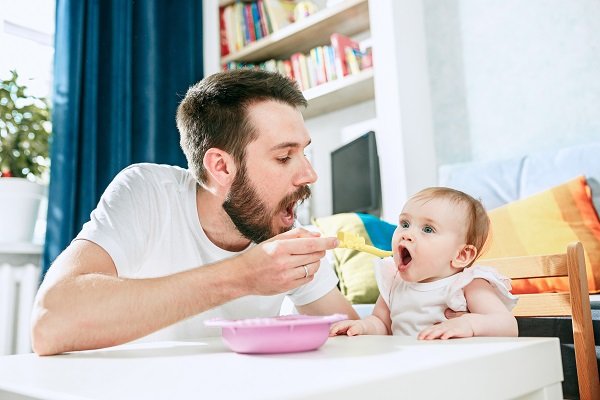 молодой папа кормит кашей малньку дочку, фото